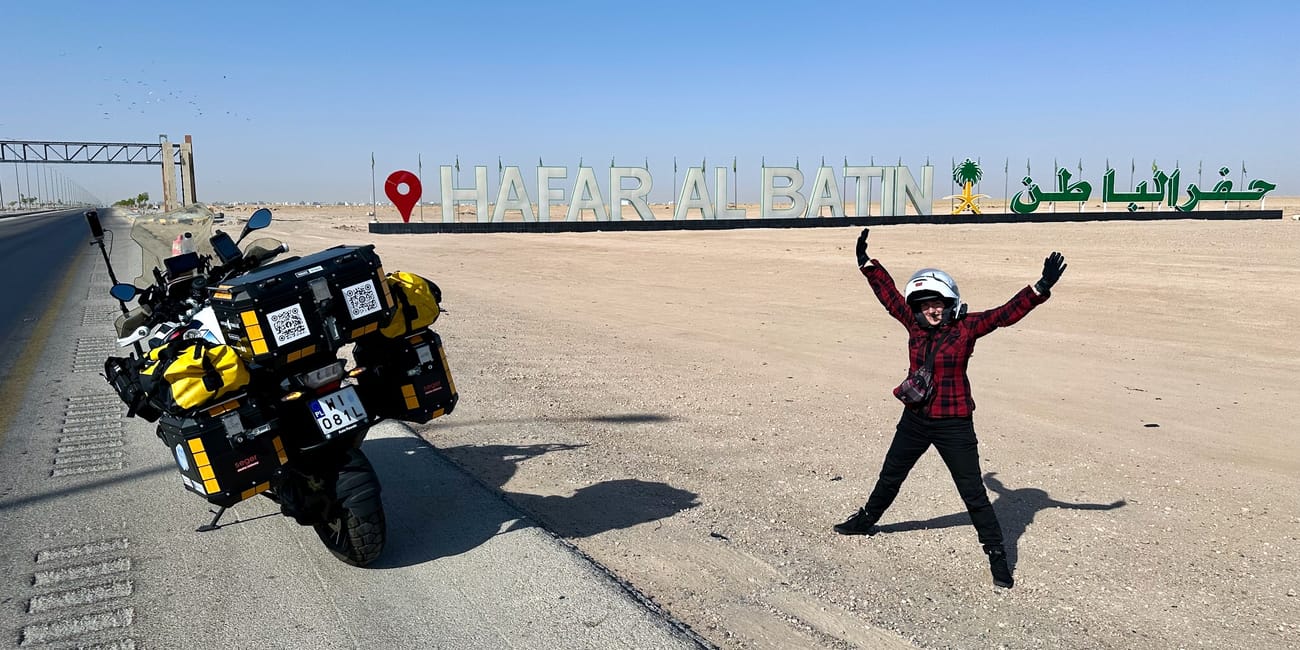 Motorcycle adventure in saudi arabia at the hafaf al batin sign with a rider cheering on the roadside