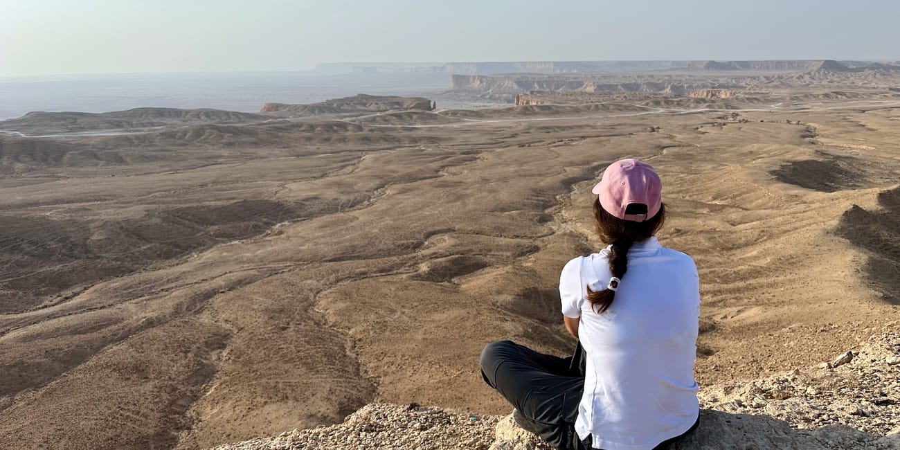 Osoba siedząca na skale nad pustynnym krajobrazem edge of the world w arabii saudyjskiej