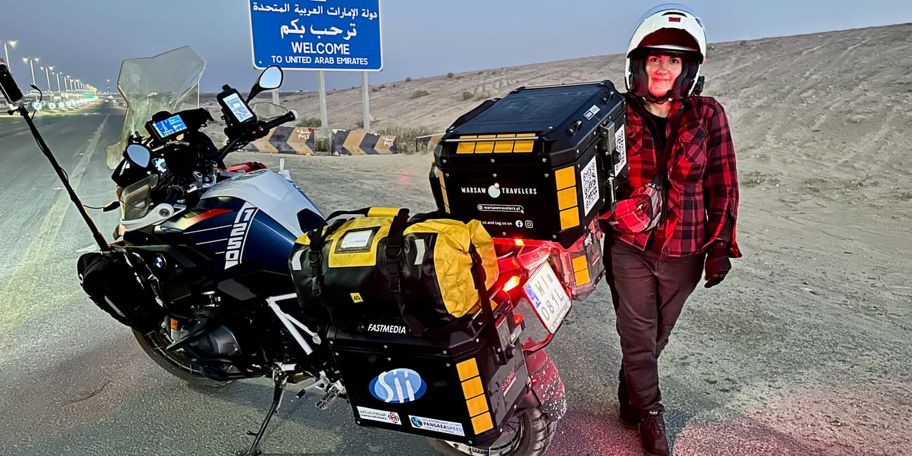 Motocykl podróżny i kierowczyni przy znaku „welcome to united arab emirates” na pustynnej drodze.