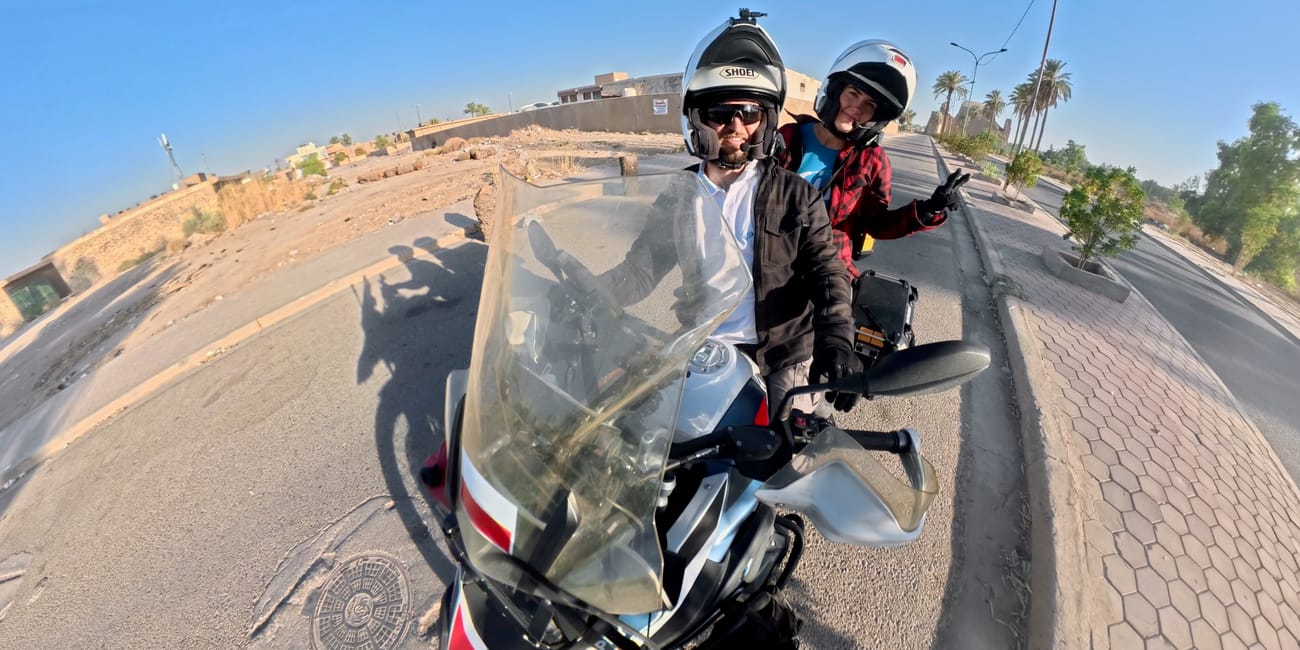 Dwóch motocyklistów pozujących na drodze w iraku przy palmach i bezchmurnym niebie.