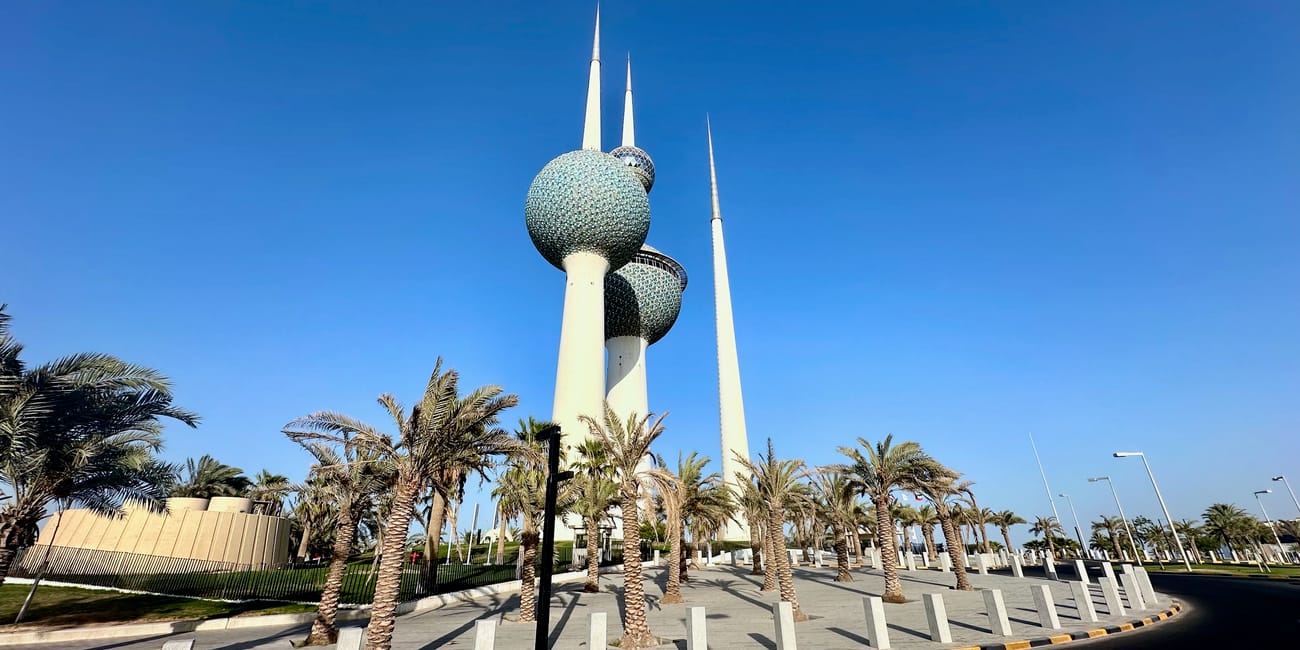 Kuwait city skyline view with the kuwait towers and palm-lined walkway under a clear blue sky
