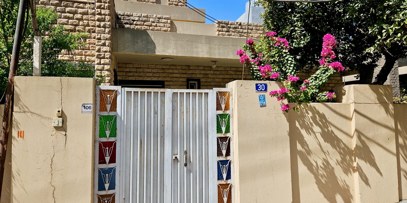 Dom w erbil city z białą bramą, kamiennym ogrodzeniem i różowymi kwiatami bougainvillei.