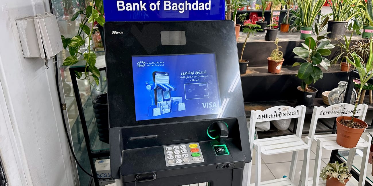 Bankomat bank of baghdad w centrum handlowym w kurdystanie, otoczony roślinami.