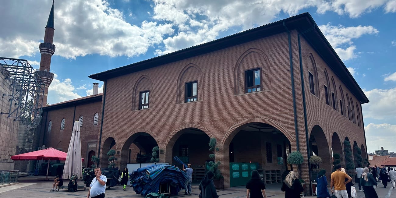 Turkey, ankara mayram mosque exterior with brick arches, minaret, and visitors under a cloudy sky