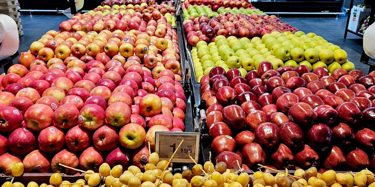 Kuwait foods market display with neatly stacked apples, dates, and grapes in bins
