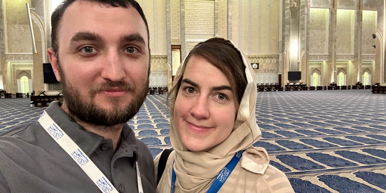 Couple taking a selfie at kuwait city grand mosque inside the ornate prayer hall with blue carpet patterns
