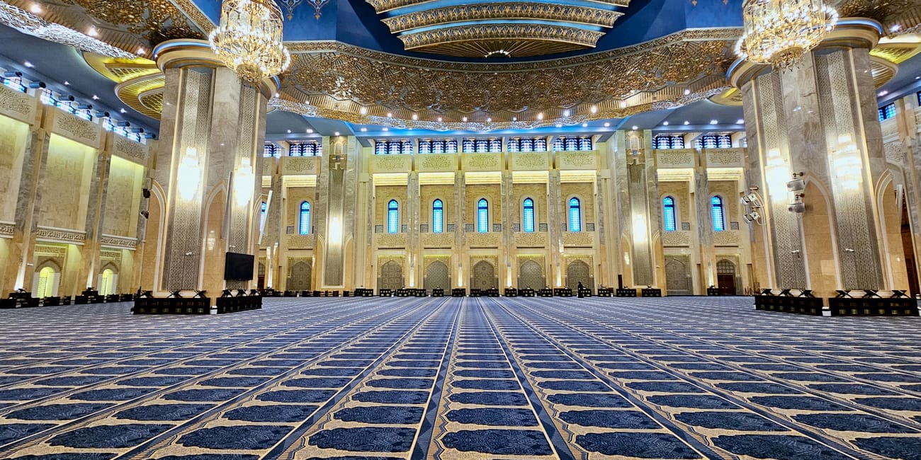 Kuwait city grand mosque interior with ornate blue ceiling, chandeliers, and patterned prayer carpet