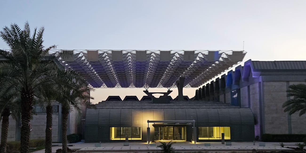 Kuwait city national museum entrance with modern facade and arched canopy, framed by palm trees at dusk