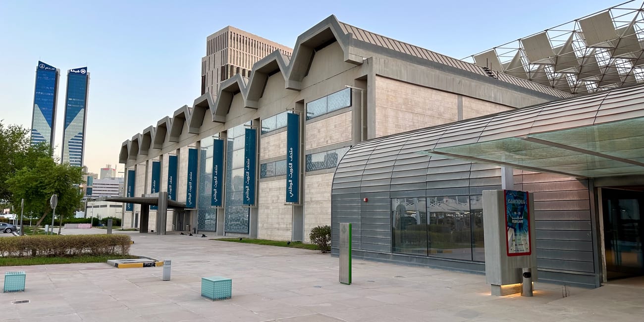 Kuwait city national museum exterior with modern stone façade, curved glass entrance, and blue banners