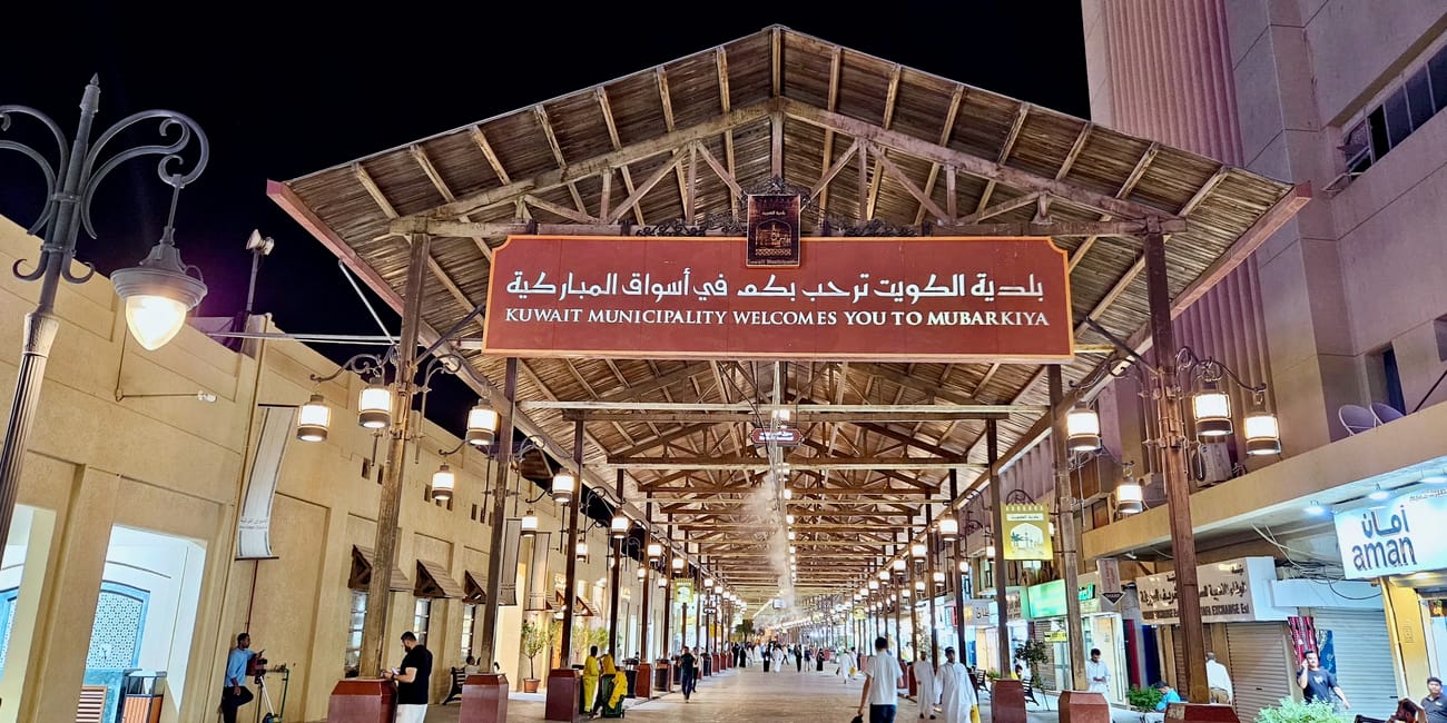 Kuwait, city al mubarakiya entrance sign over a covered walkway with warm lights and shoppers at night