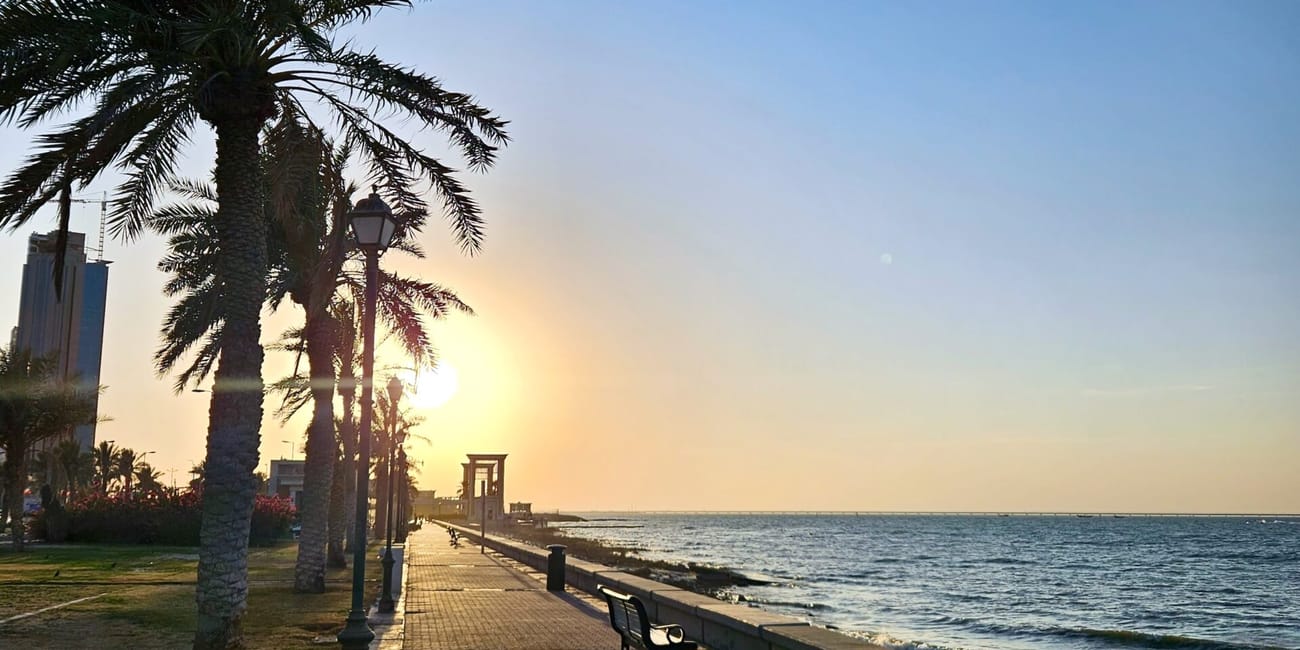 Kuwait city waterfront promenade with palm trees and benches along the shoreline at sunset