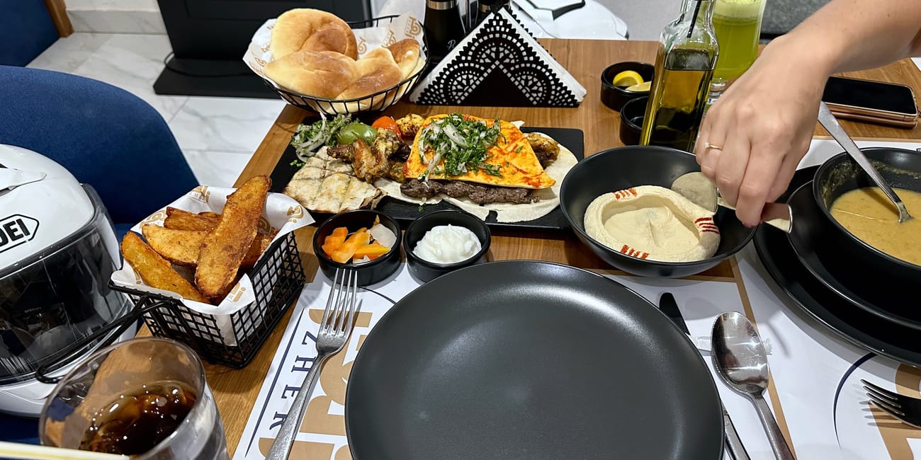 Stół w restauracji muscat foods w omanie z hummusem, pieczywem, mięsem z grilla, frytkami i napojami.