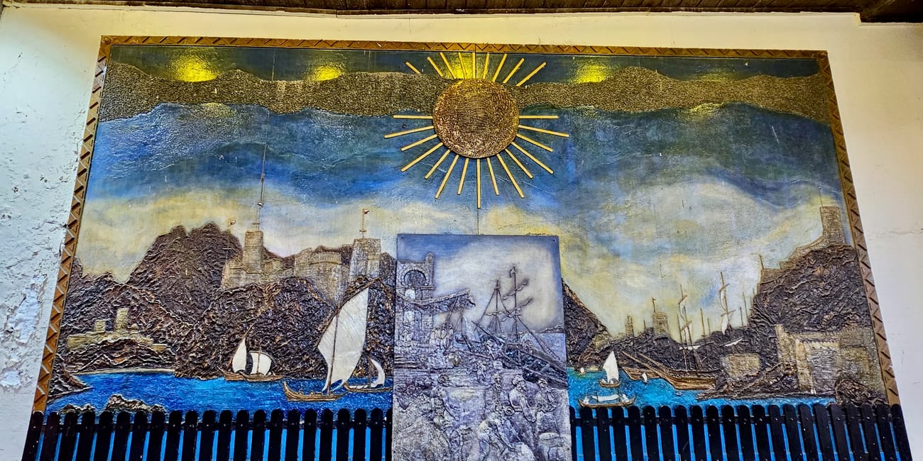 Malowidło w muscat muttrah souq w omanie, przedstawiające port, łodzie, góry i słońce nad zatoką