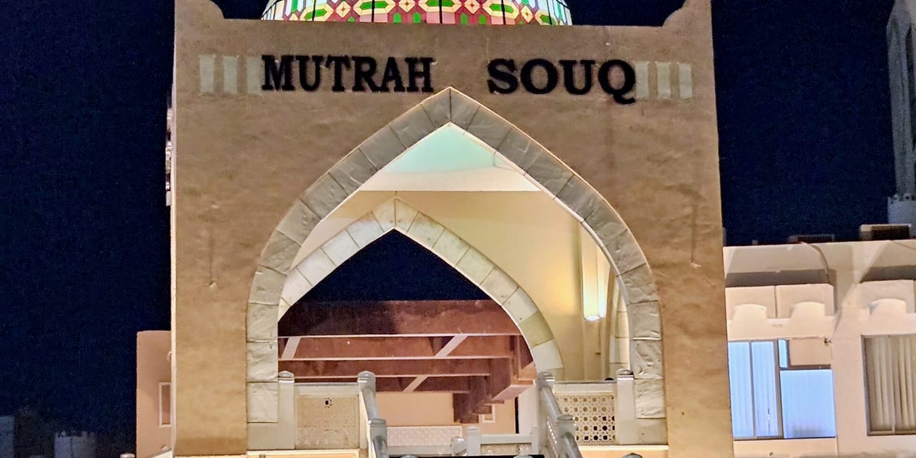 Wejście do mutrah souq w muskacie nocą, z łukowym portalem i kolorową kopułą nad budynkiem.