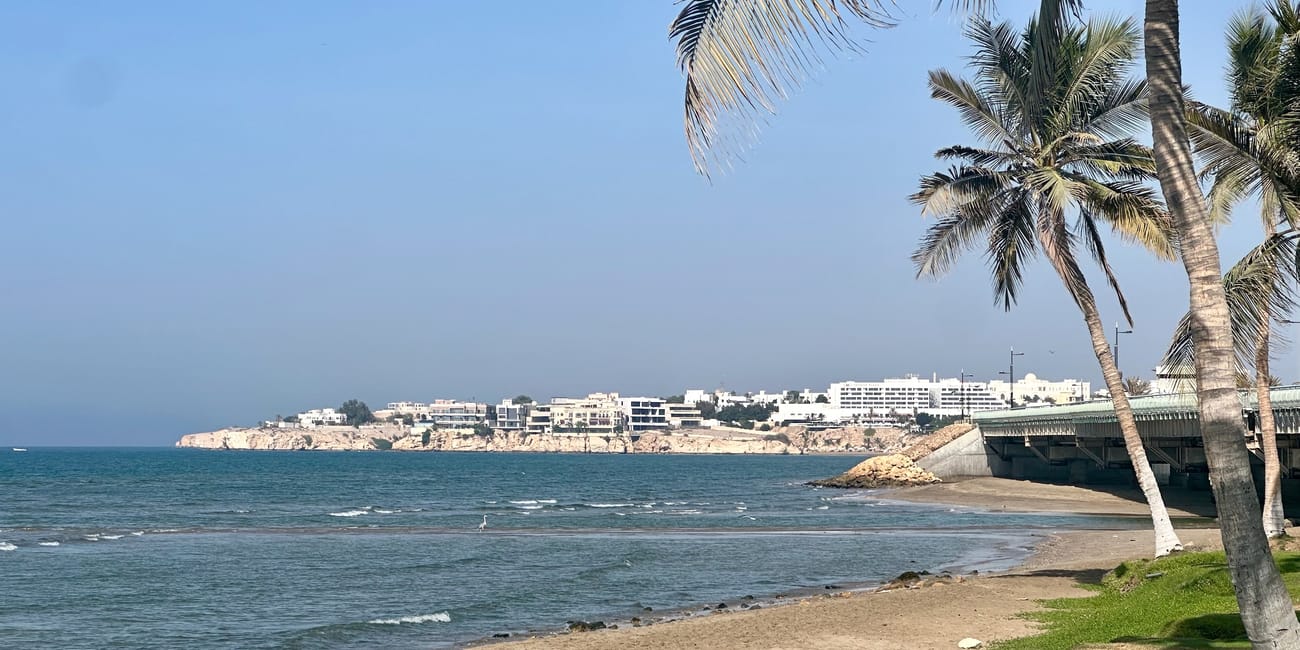 Plaża qurum w muskacie w omanie, spokojne morze, palmy i zabudowa na skalistym wybrzeżu