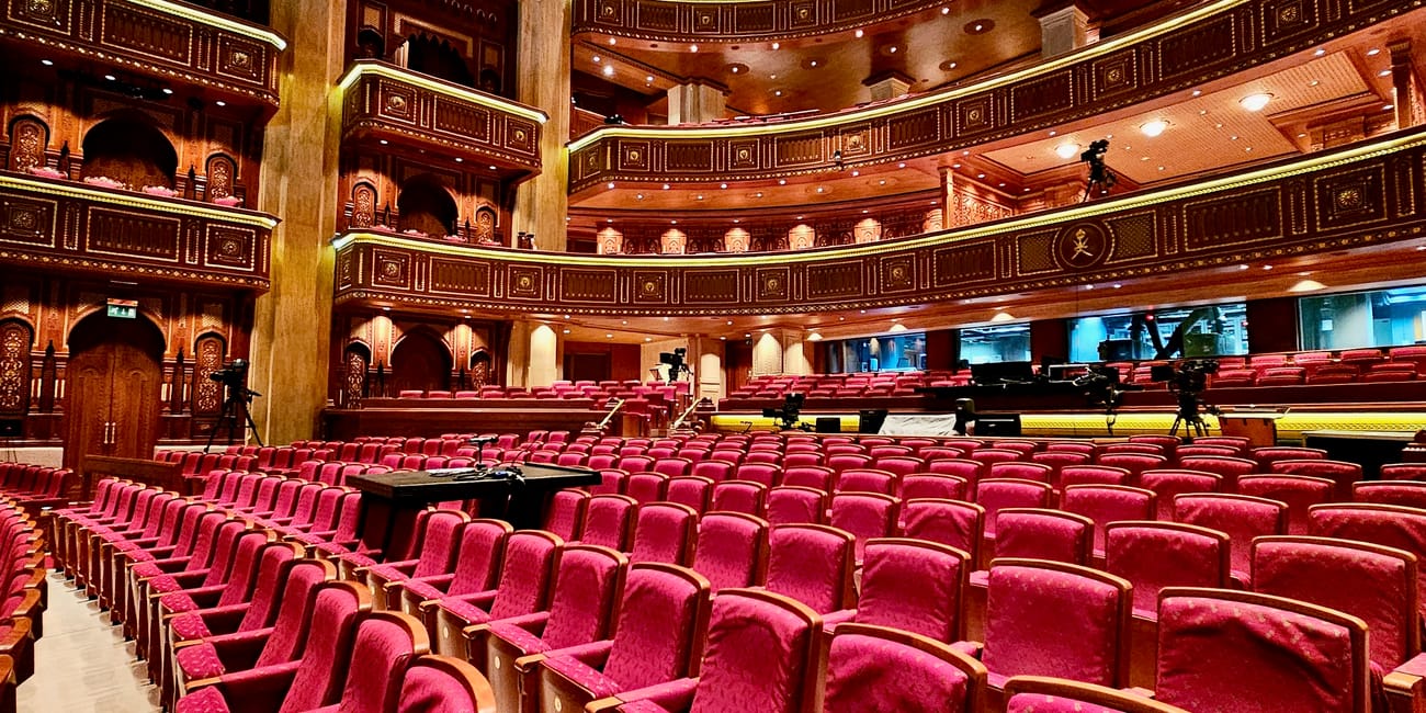 Wnętrze muscat royal opera house w omanie z rzędami czerwonych foteli i bogato zdobionymi balkonami