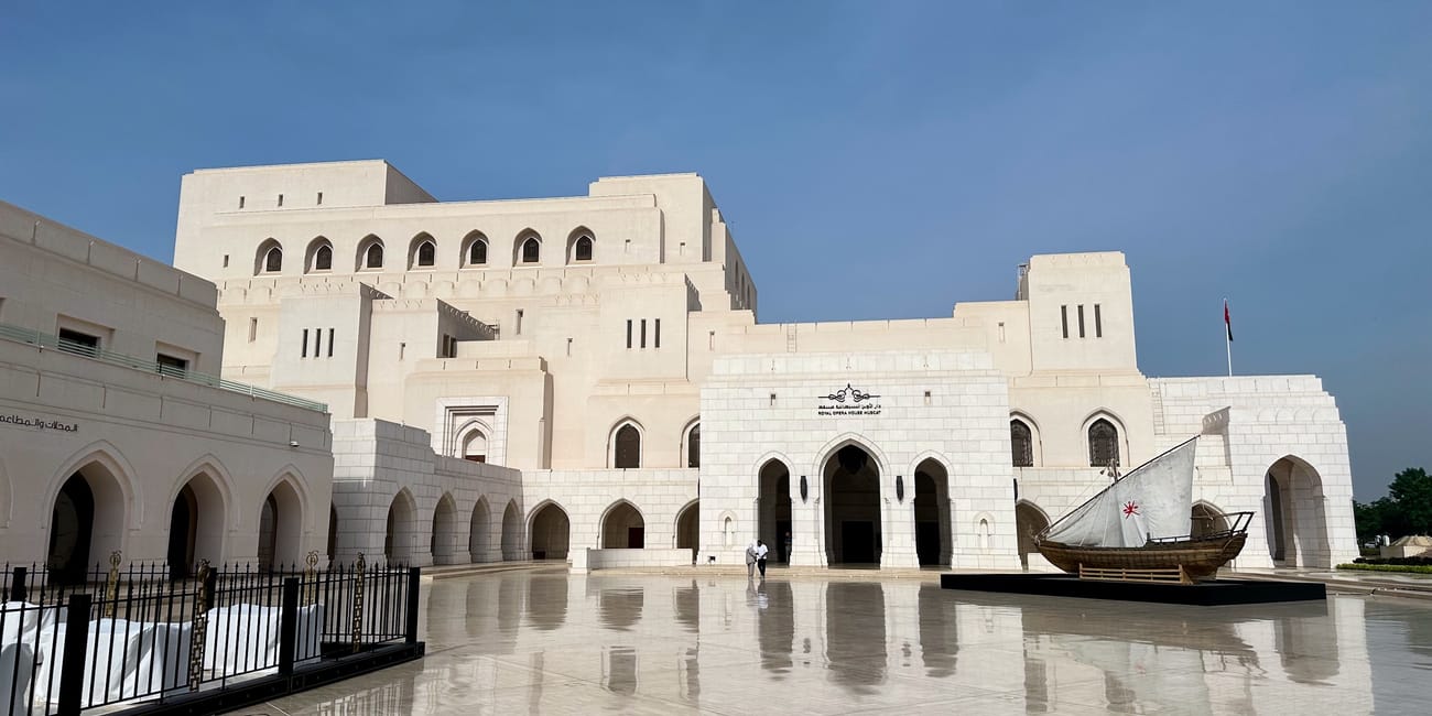 Royal opera house muscat w omanie, jasny gmach z arkadami i łodzią na dziedzińcu po deszczu
