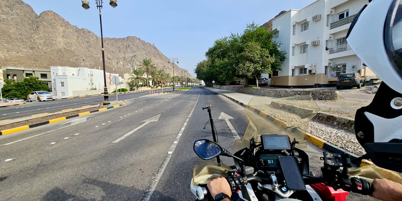 Ulica w muscat w omanie, widok z motocykla na szeroką drogę między górami i białymi budynkami