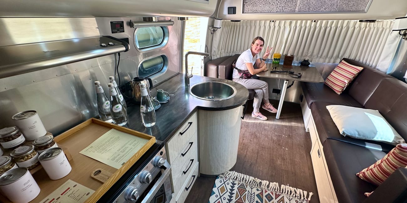 Interior of saudi arabia’s al ula caravans by habitas with a kitchenette, seating, and a woman posing by a table