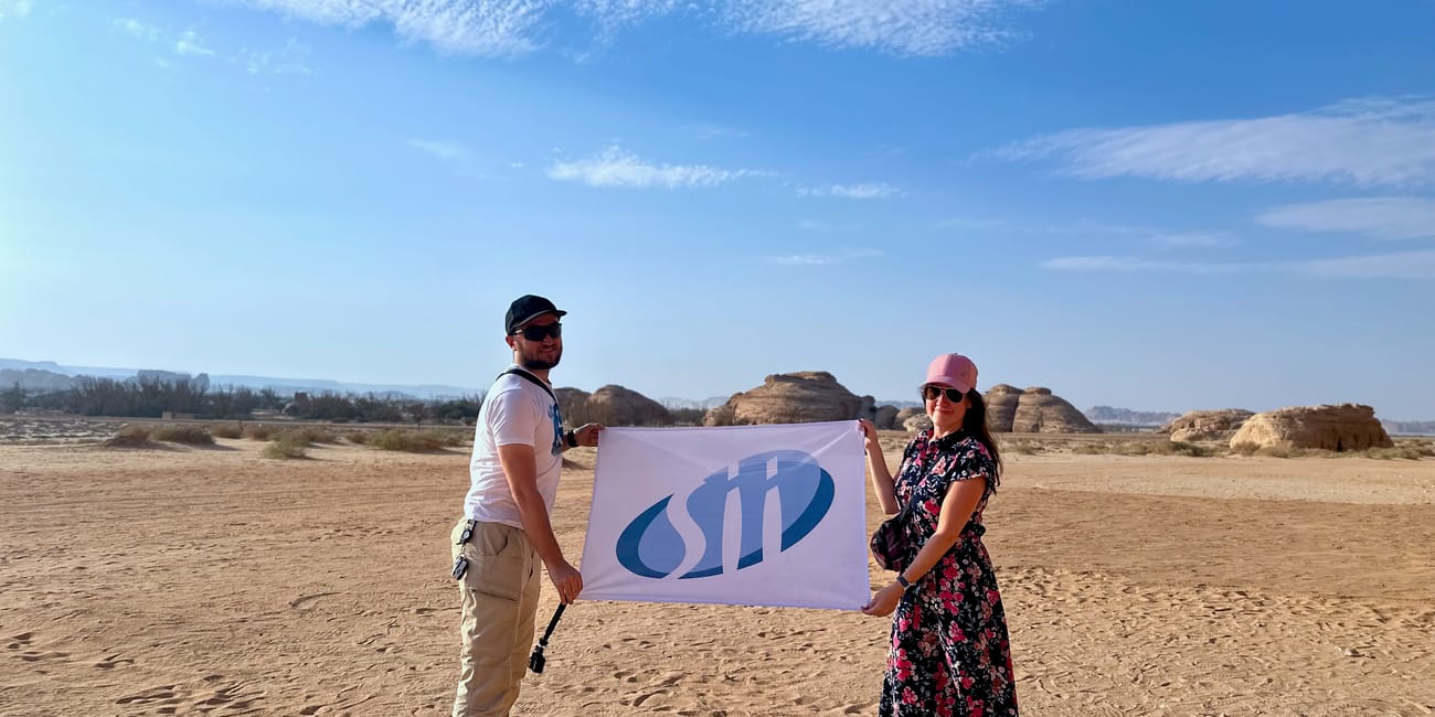 Tourists holding a banner in al ula filip and jadwiga, saudi arabia, with desert rocks under a blue sky