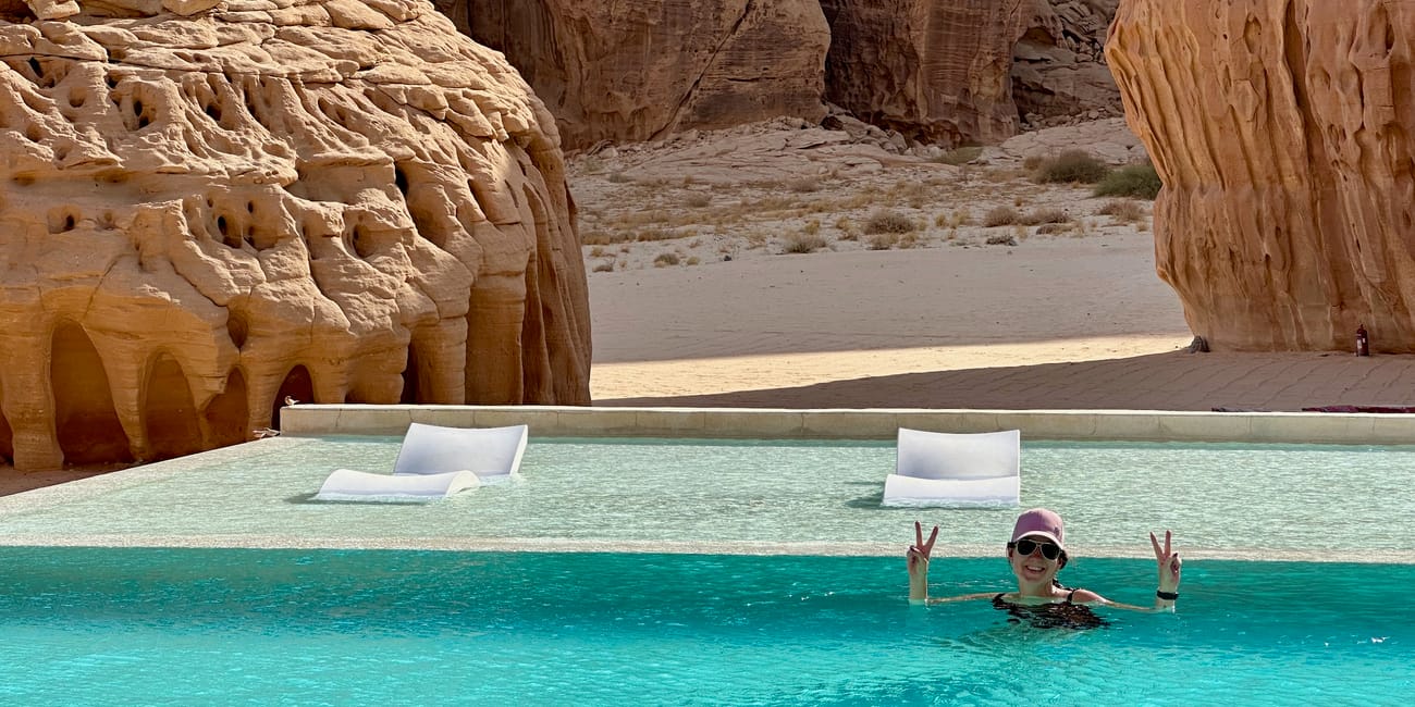 Woman swimming in a turquoise pool at al ula habitas, saudi arabia, with desert rock cliffs in the background