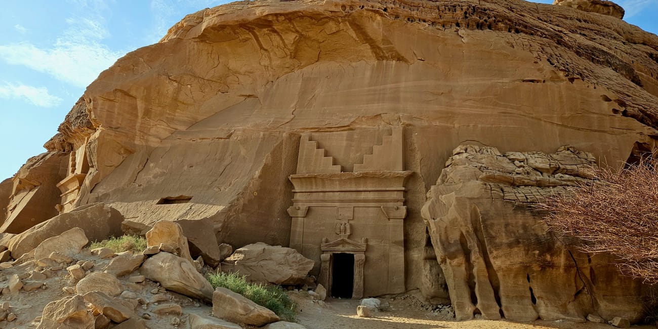Alula hegrа rock-cut tomb entrance with carved stone facade under a blue sky