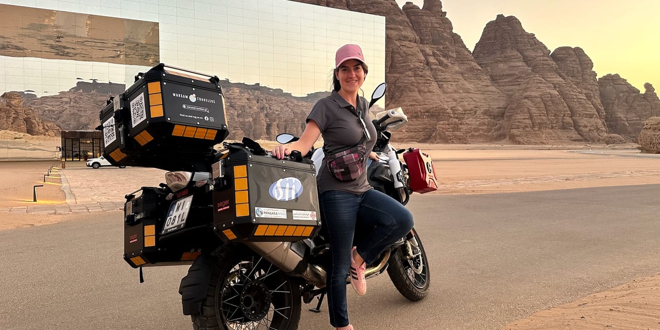 Woman posing with a touring motorcycle at al ula maraya, saudi arabia, with desert rock formations in the background