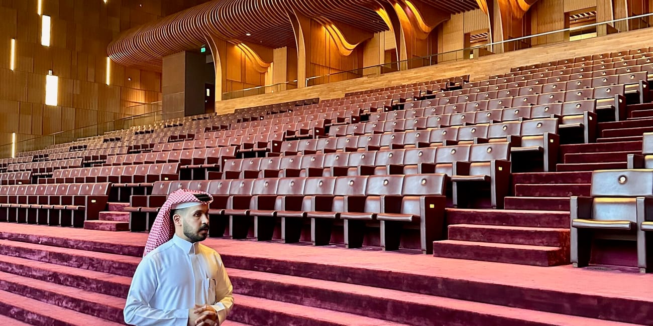 Saudi arabia, al ula maraya inside: man in white thobe standing in a grand auditorium with curved golden ceiling lights