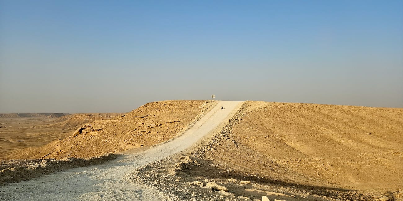 A winding track across dunes at saudi arabia’s edge of the world under a clear blue sky
