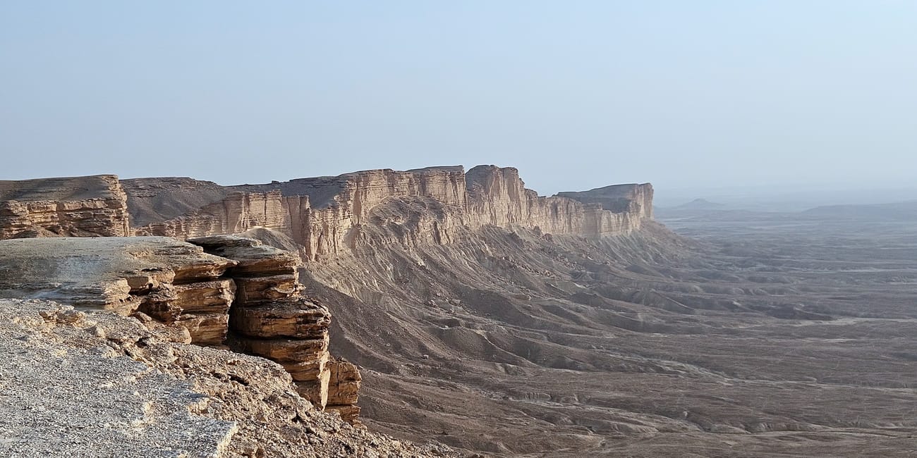 Klify edge of the world w arabii saudyjskiej nad rozległą pustynną doliną pod jasnym niebem
