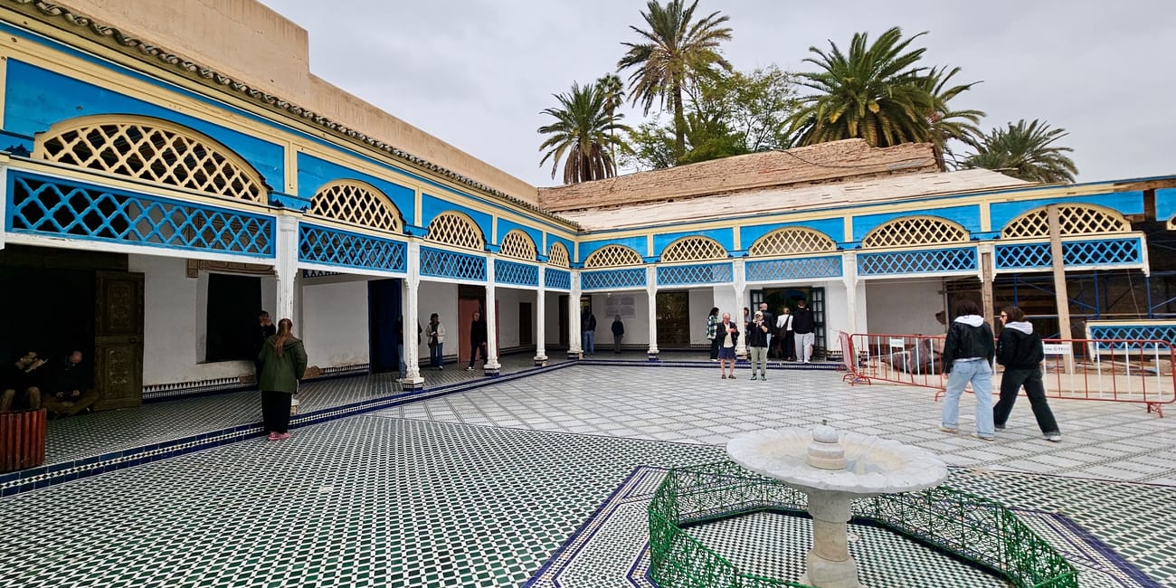 Marrakech bahia palace courtyard with blue-and-white arches, patterned tile floor, and visitors