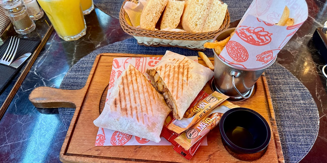 Marrakech foods table setting with grilled sandwiches, bread basket, orange soup, and juice drinks