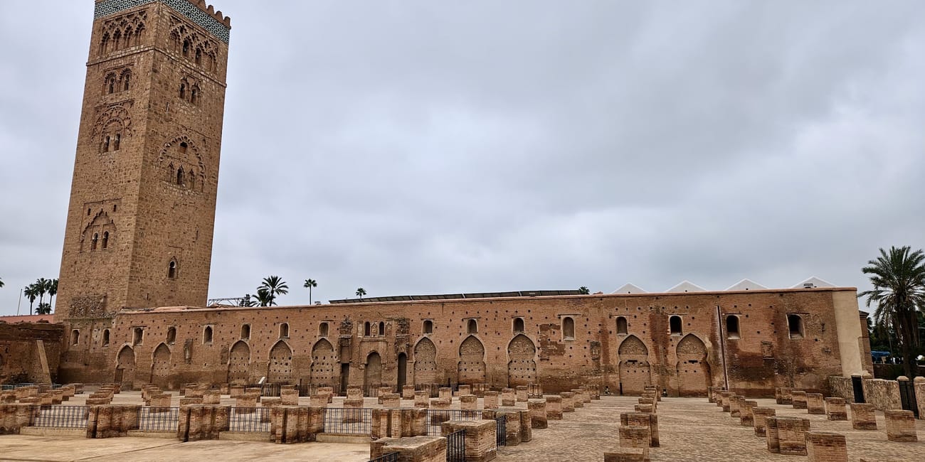 Marrakesh’s koutoubia mosque minaret and courtyard with stone arches under an overcast sky