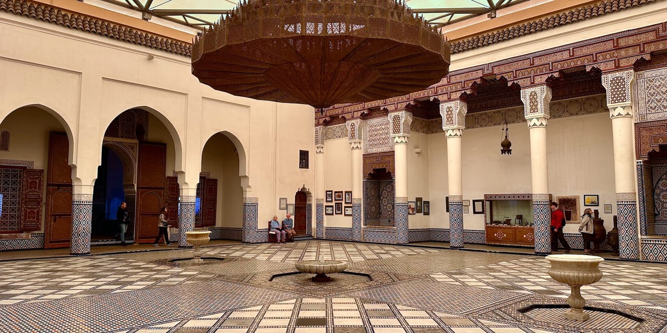 Morocco museum in marrakech, with patterned tiled floor, white arches, and ornate wooden canopy in the courtyard