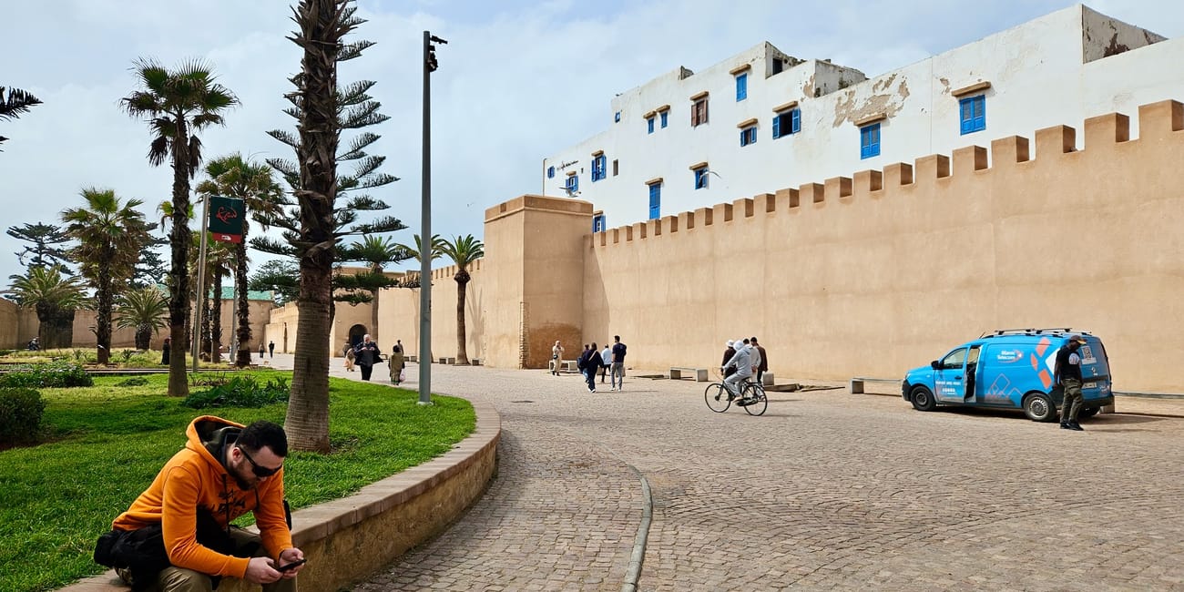 Essaouira, medyna w maroku: dziedziniec z białymi murami i niebieskimi okiennicami, ludzie i samochód przy bruku