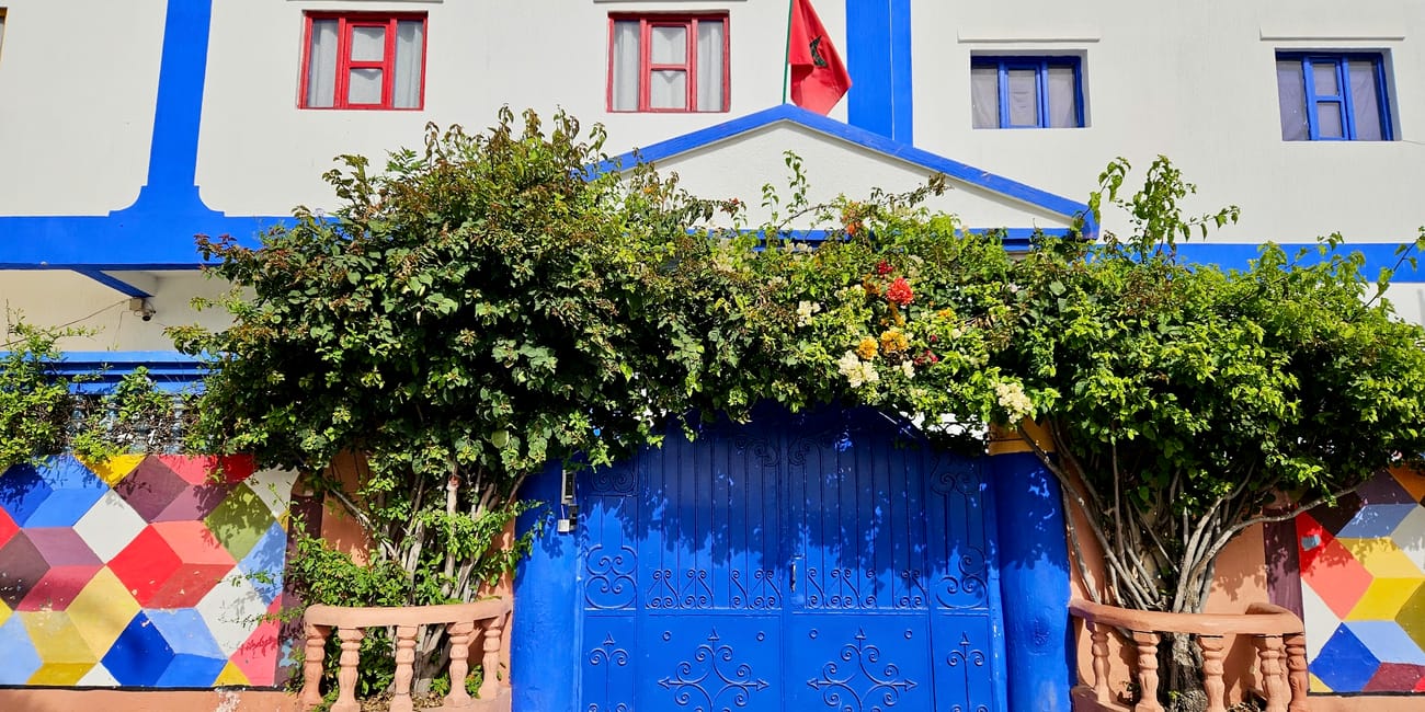 Morocco essaouira: szkolny budynek z niebieskimi drzwiami i flagą na tle zielonych krzewów