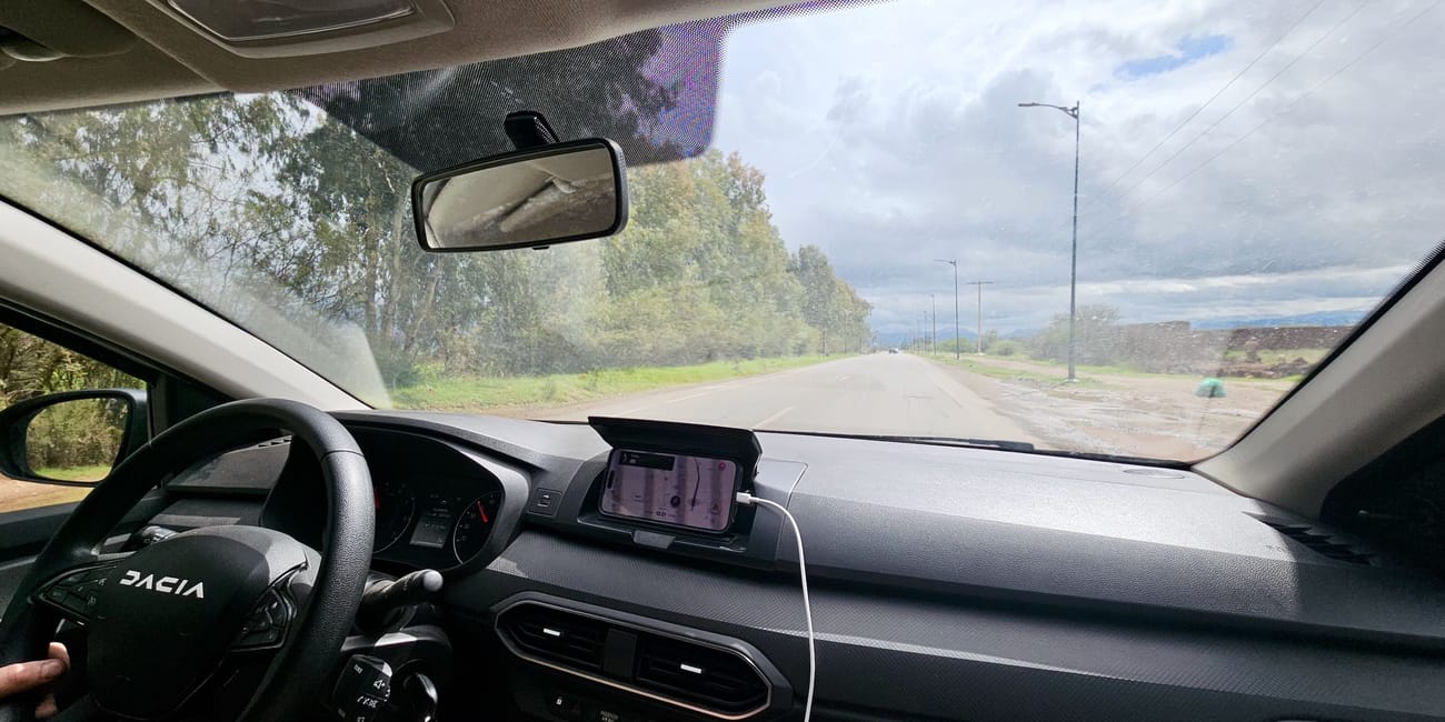 Widok z wnętrza samochodu dacia na drogę w maroku, przed maską widać prostą szosę i pochmurne niebo
