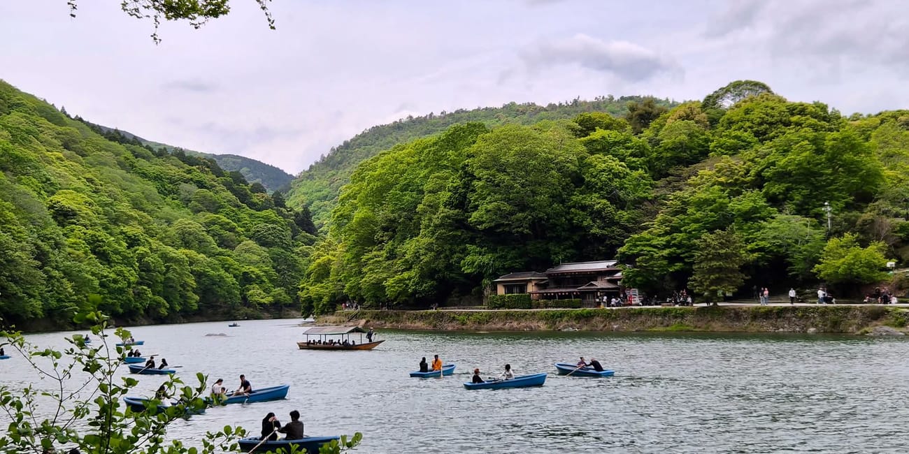 Most togetsukyo w kioto z łódkami na rzece i zielonymi wzgórzami w tle