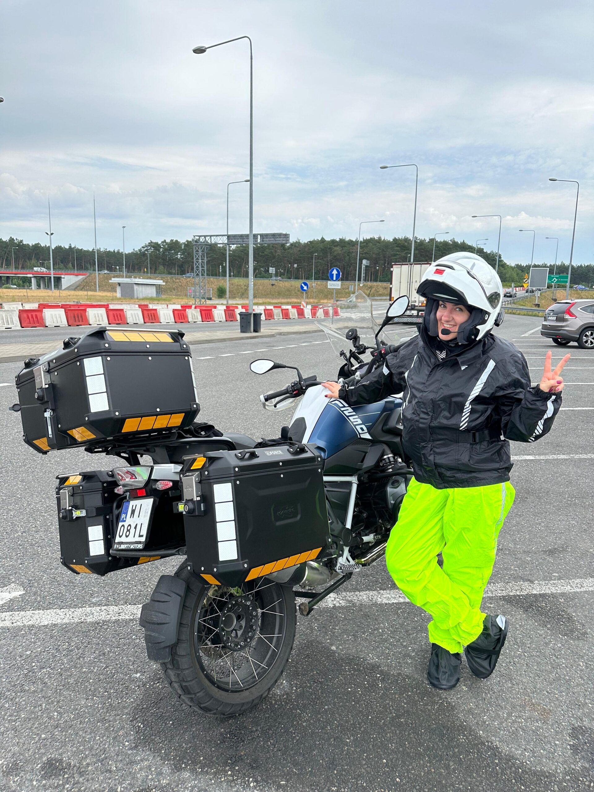 Kobieta w kasku stoi przy motocyklu turystycznym na parkingu w niemczech.