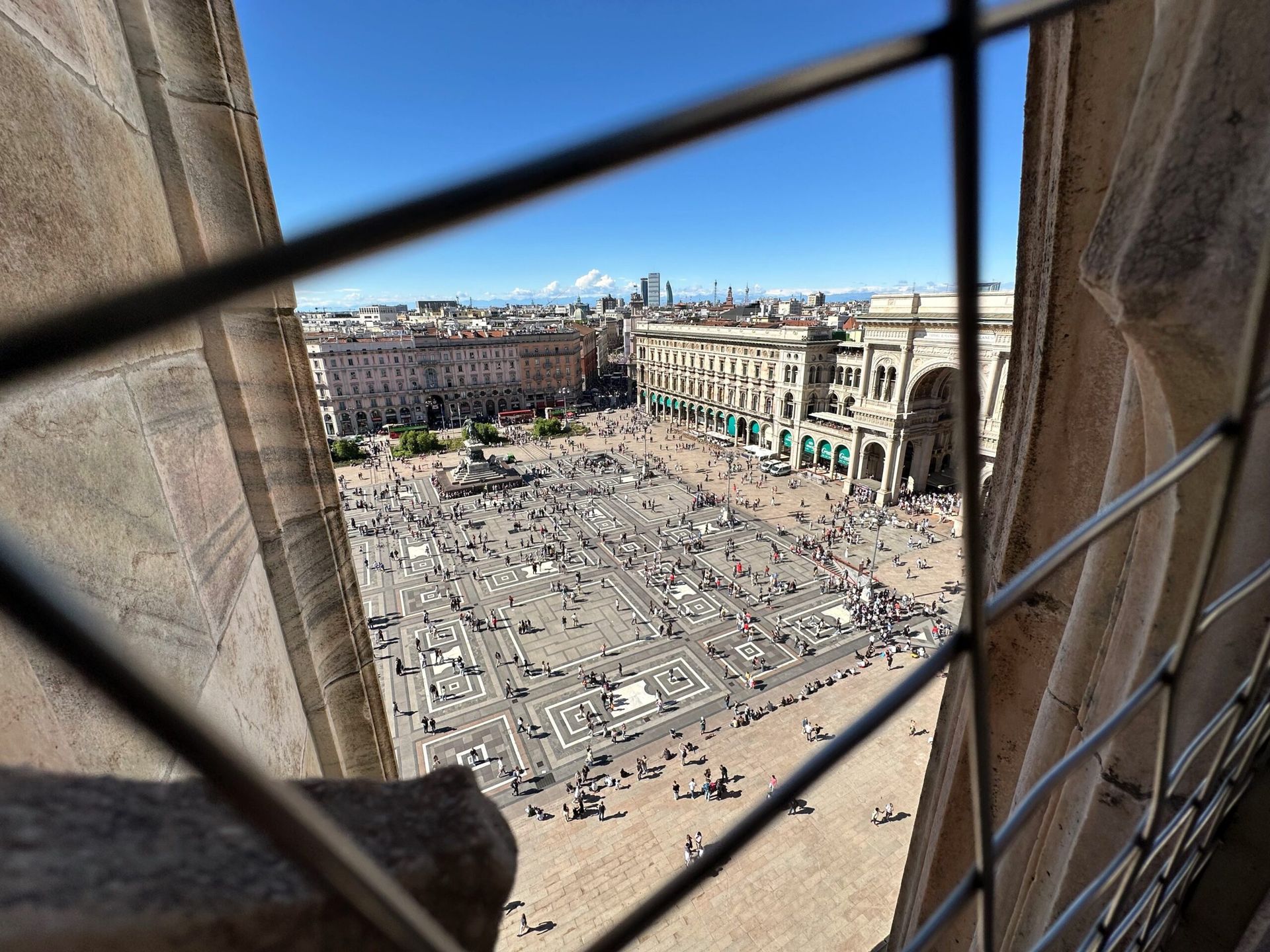 Widok na piazza del duomo w mediolanie z góry, przez kamienne okno katedry.