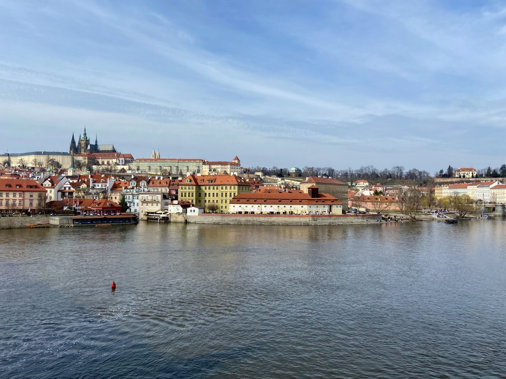 Panorama pragi nad wełtawą z zamkiem praskim i czerwonymi dachami.