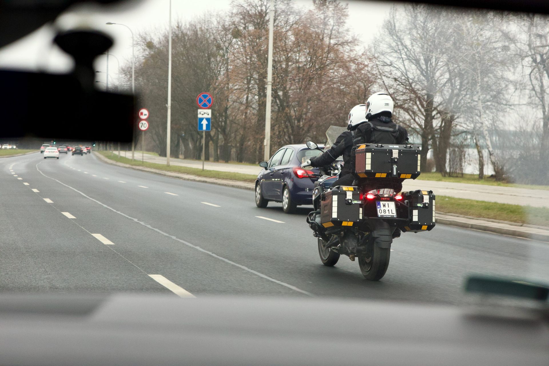 Dwóch motocyklistów jedzie ulicą w warszawie, z kuframi i białymi kaskami.