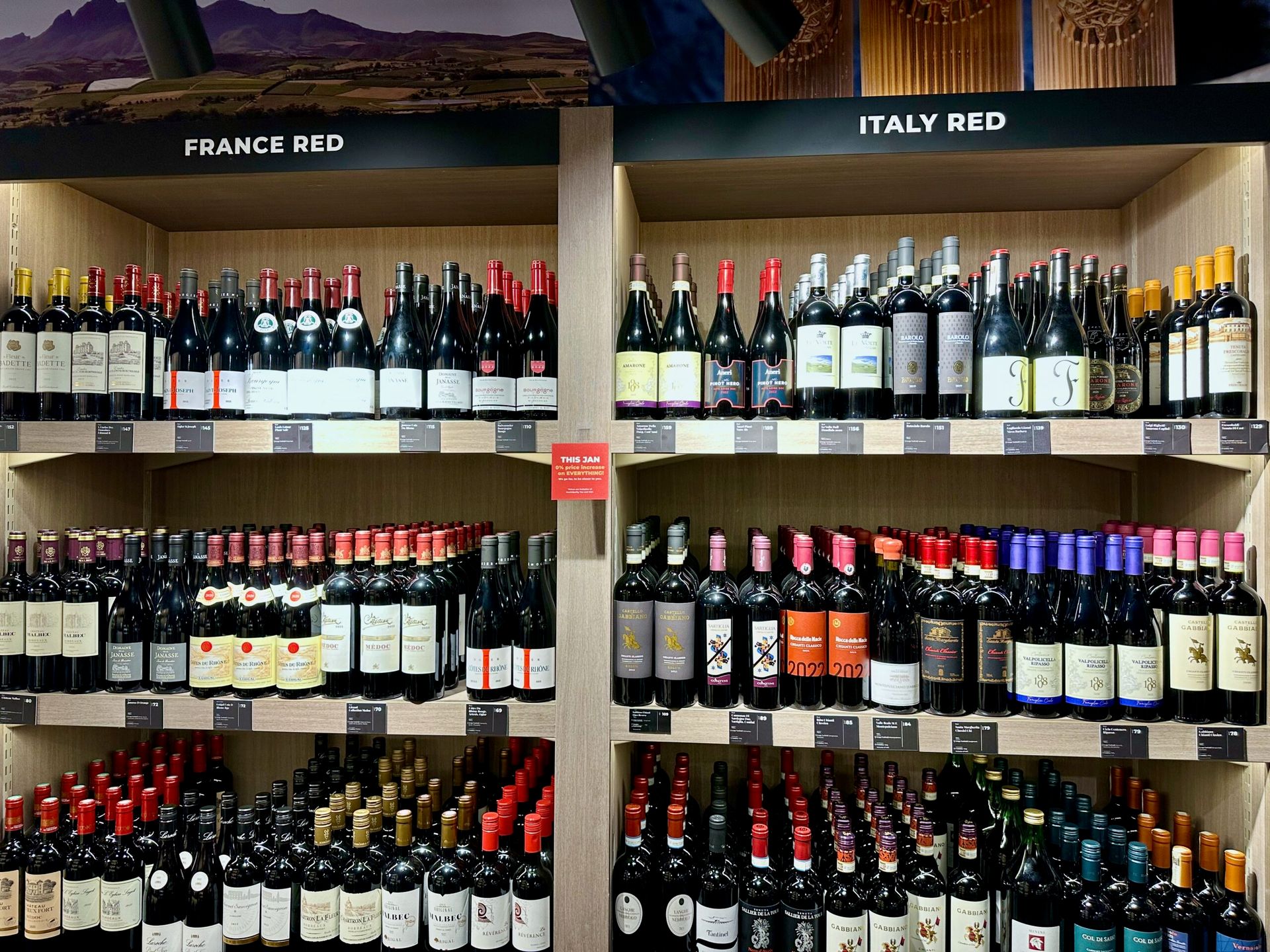 Półki z czerwonym winem w sklepie, z oznaczeniami france red i italy red.