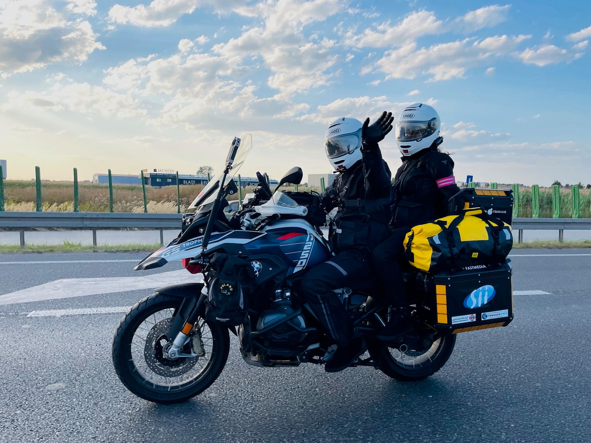 Dwoje motocyklistów na turystycznym motocyklu na trasie w desert horizons, jedno macha do kamery.