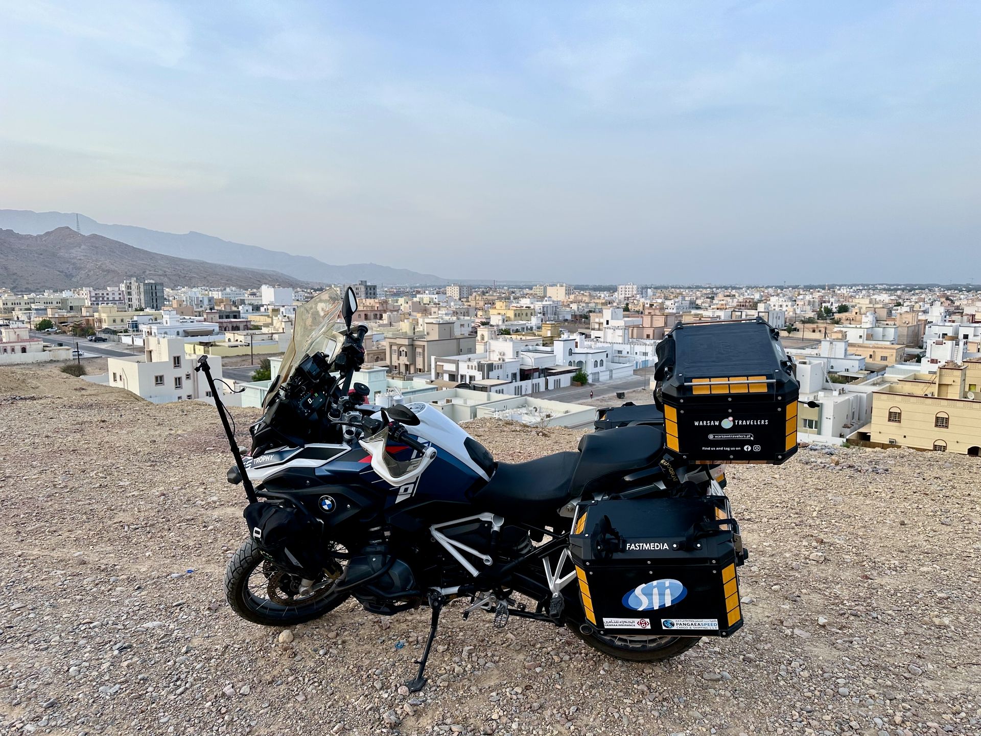 Motocykl turystyczny na wzgórzu nad miastem w omanie, z panoramicznym widokiem na zabudowę i góry.