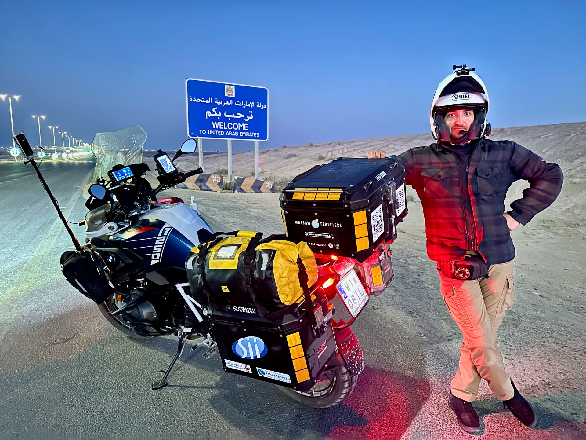 Motocyklista z wyprawowym bmw przy znaku al ghuwaifat land border witającym w zjednoczonych emiratach arabskich