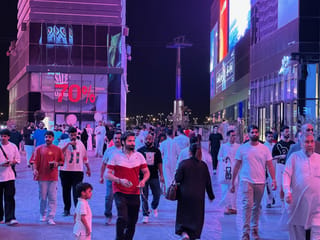 Tłum ludzi spaceruje nocą między neonowymi budynkami w arabii saudyjskiej.