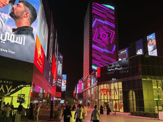 Nighttime shopping district in saudi arabia with people walking past bright led billboards.
