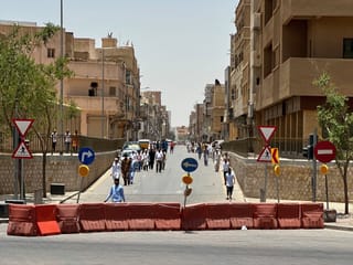 Street in saudi arabia with people walking past road barriers and traffic signs