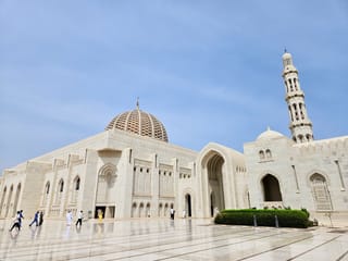 Wielki meczet sułtana kabusa w muskacie, biały budynek z kopułą i wysokim minaretem przy rozległym dziedzińcu